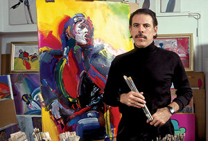 Peter stands in front of his painting of Mick Jagger while holding a paintbrush.